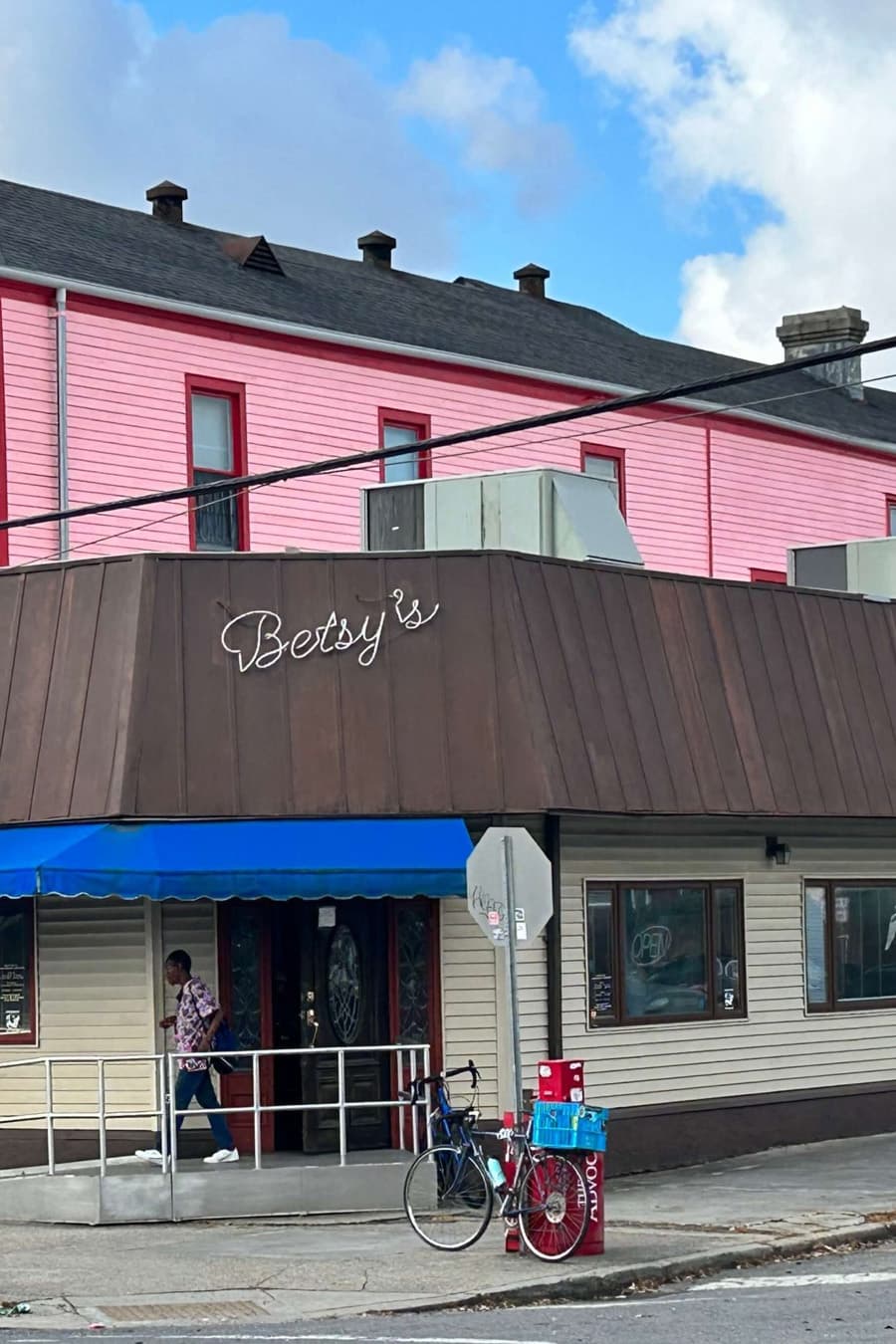 Betsy's restaurant features a brown awning, blue canopy, and a person walking past a parked bicycle.
