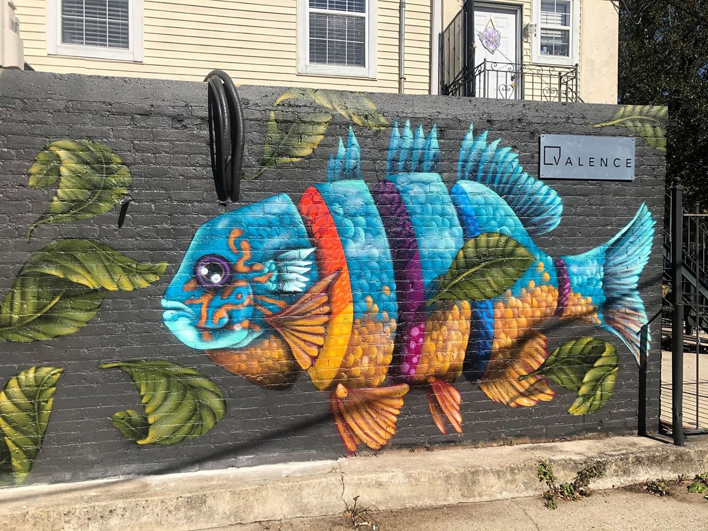 A colorful mural of a fish surrounded by green leaves on a brick wall.
