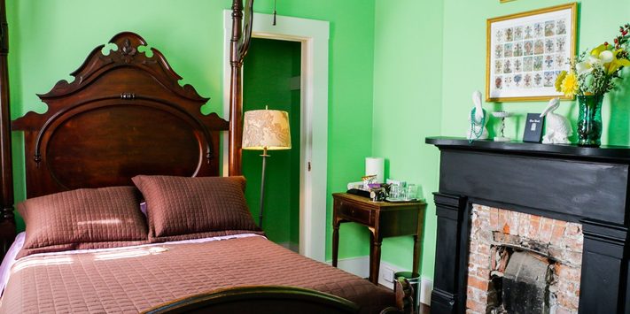 A cozy bedroom with a green wall, featuring a dark wood bed, a lamp, a fireplace, and decorative elements.
