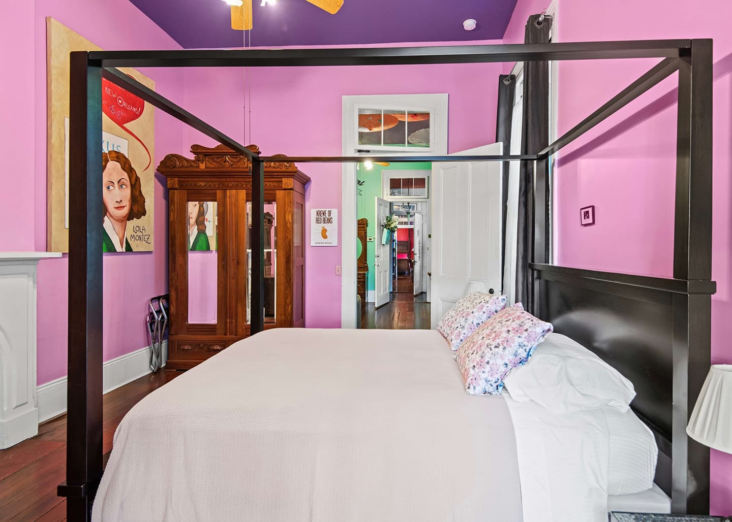 A modern four-poster bed in a brightly colored pink room, featuring eclectic decor and historical artwork.