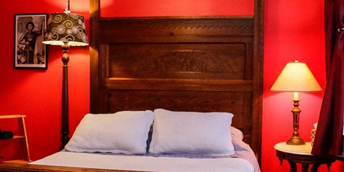 A cozy bedroom featuring a wooden bed with light blue pillows, two lamps, and red walls.