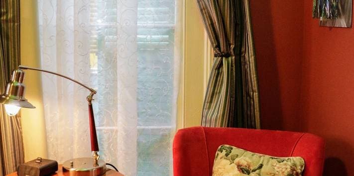 Cozy reading nook with a red armchair, a lamp, and patterned curtains by a sunny window.