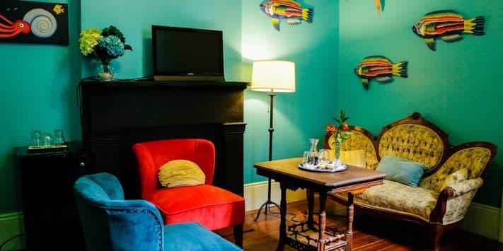 Colorful living room with a blue wall, various fish decorations, an armchair, a vintage sofa, and a small table with glassware.