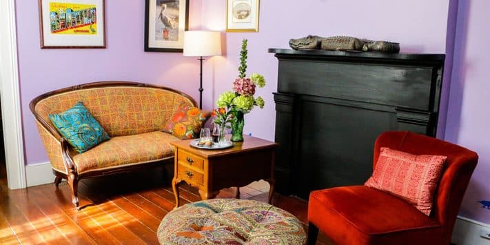 A cozy living room with a purple wall, vintage sofa, red chair, and decorative elements.