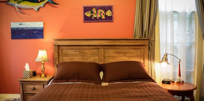 A cozy bedroom featuring a brown quilted bedspread, wooden furniture, and orange walls adorned with artwork.