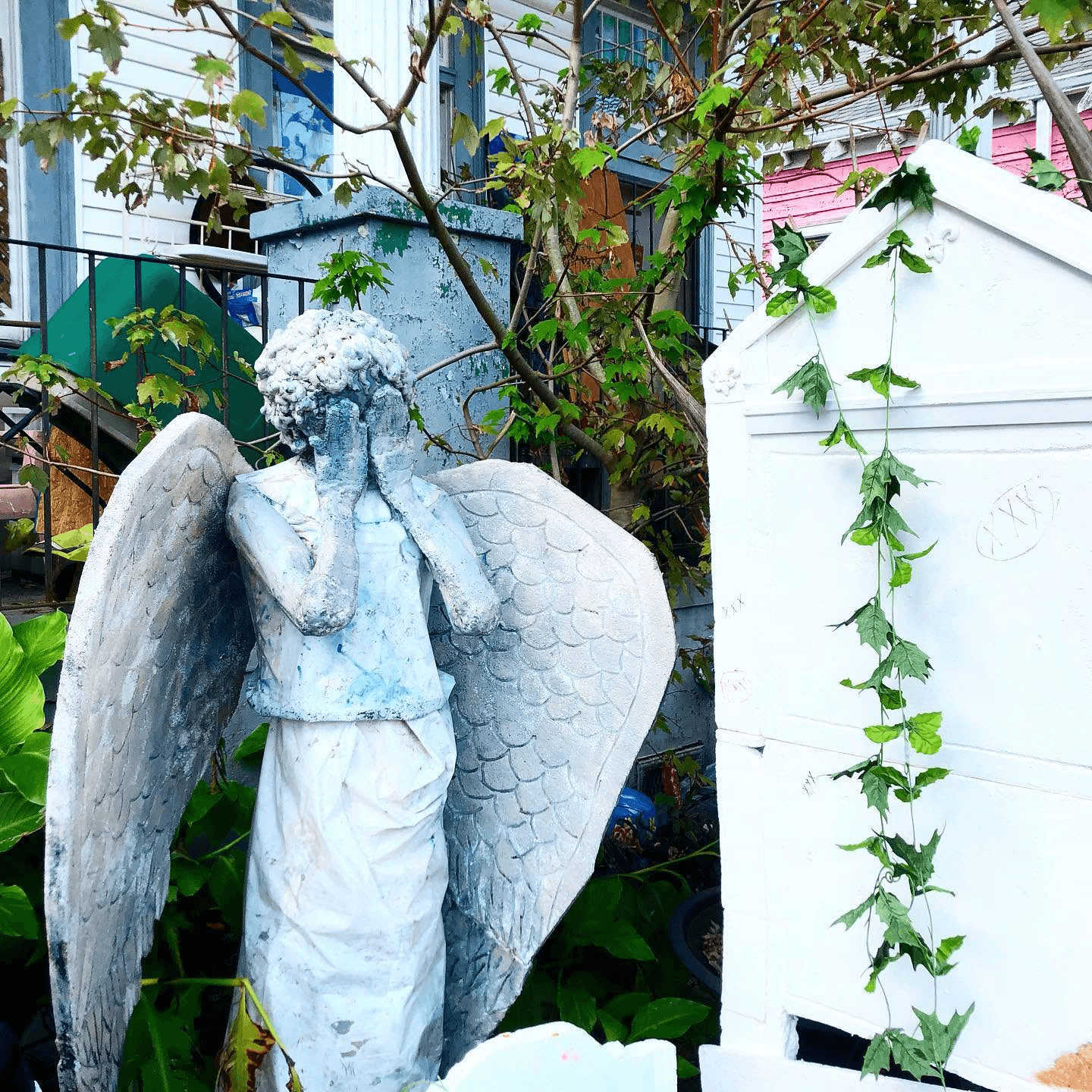 A stone angel statue covers its face beside a white structure with trailing ivy.