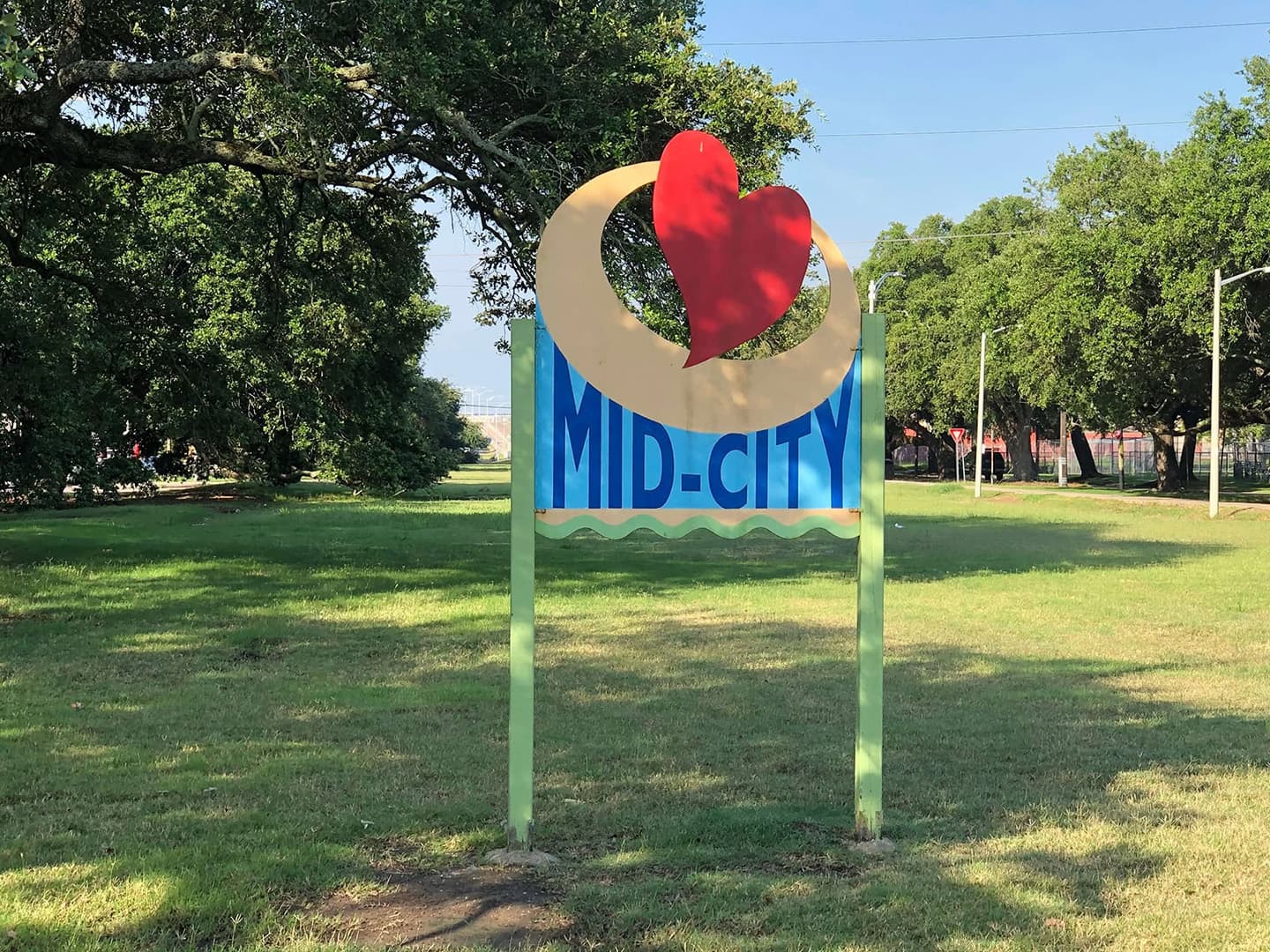 Colorful sign for "Mid-City" featuring a heart and whimsical design against a grassy background.