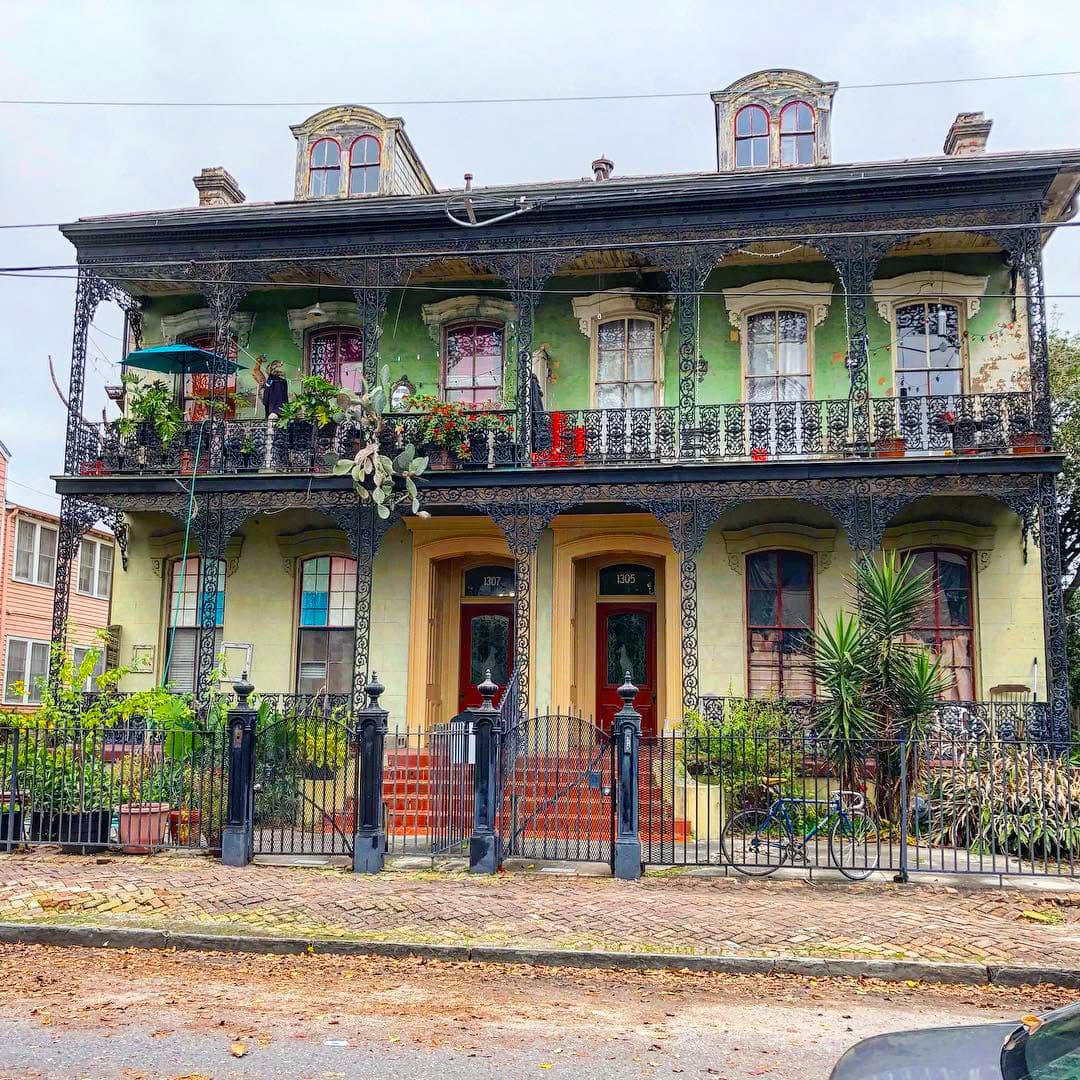 Ornate green and cream house with wrought iron balconies and colorful flowers in front.