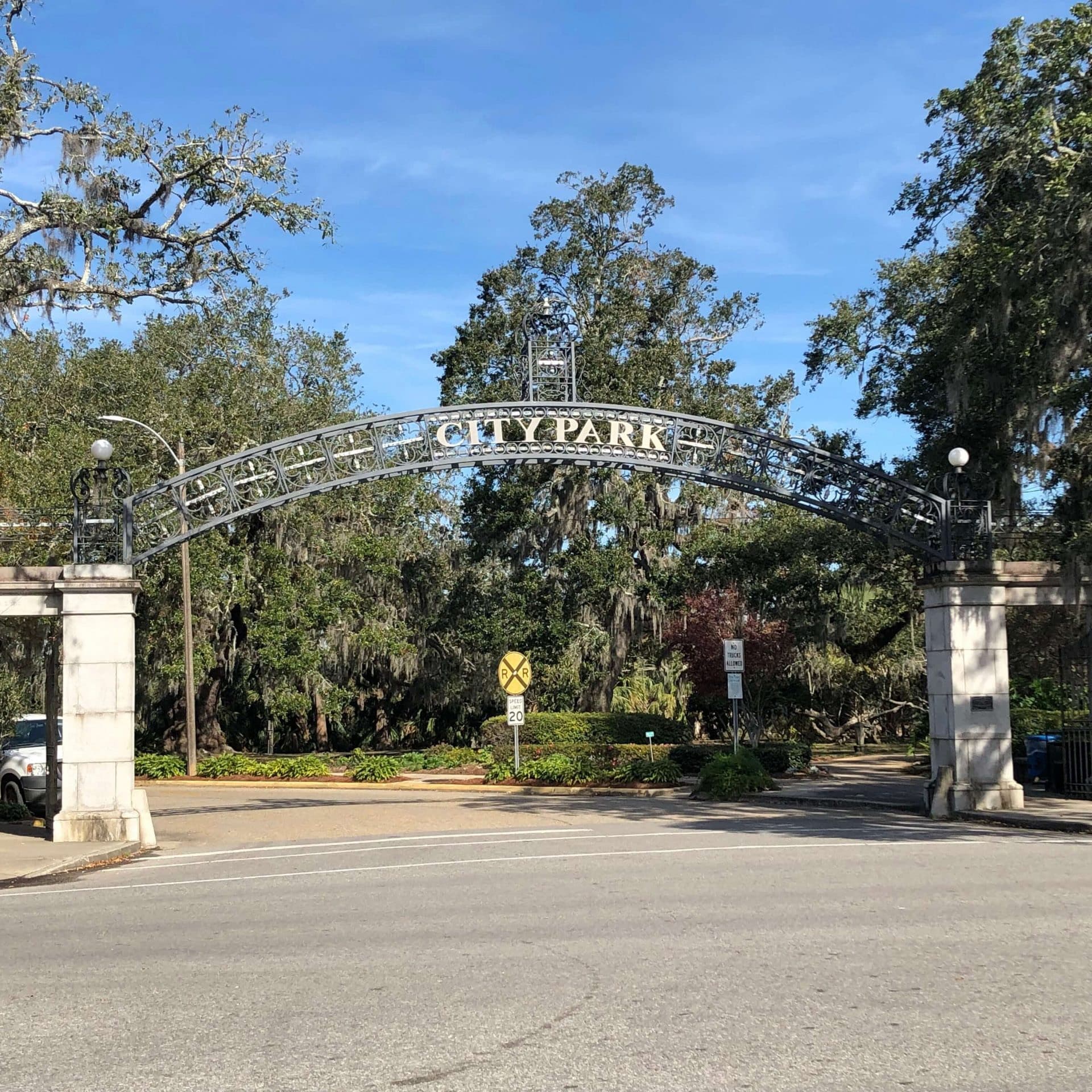 A wrought iron archway with the words "CITY PARK" spans the entrance to a green park area.