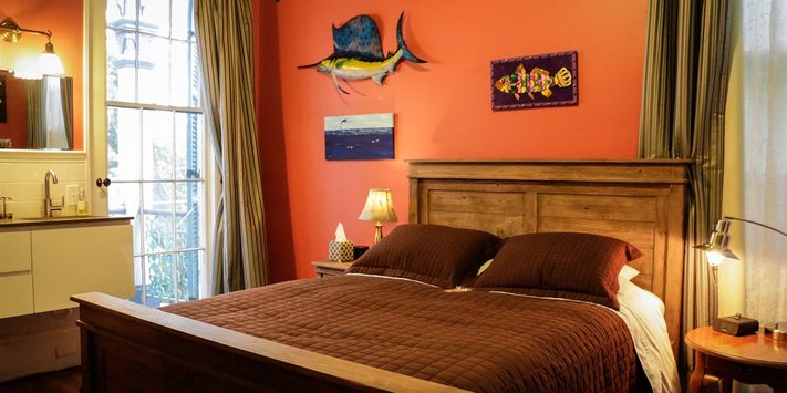 A cozy bedroom with a wooden bed, orange walls, and decorative fish artwork.