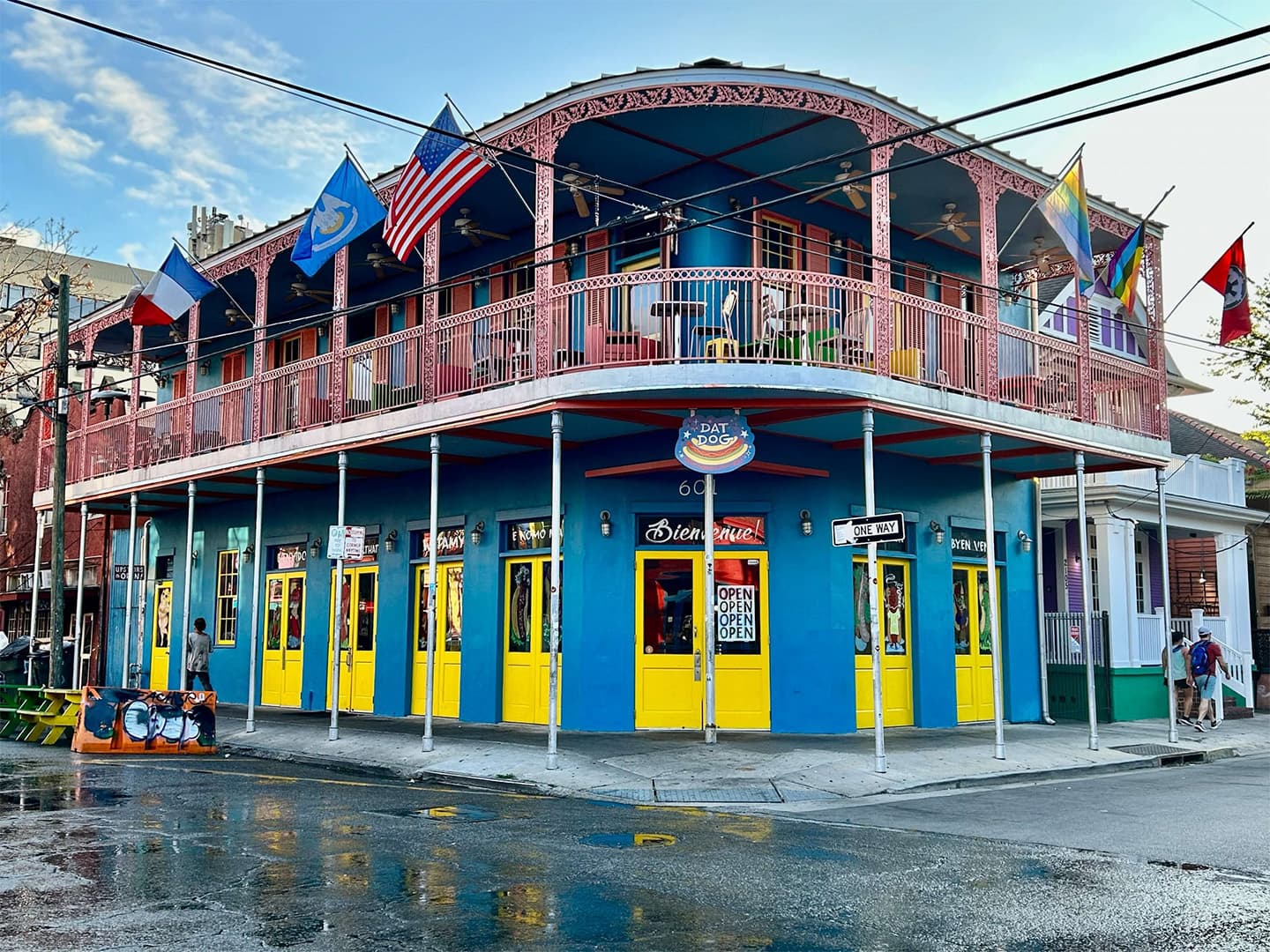 Colorful building with yellow doors and flags, featuring a balcony and a reflection on wet pavement.