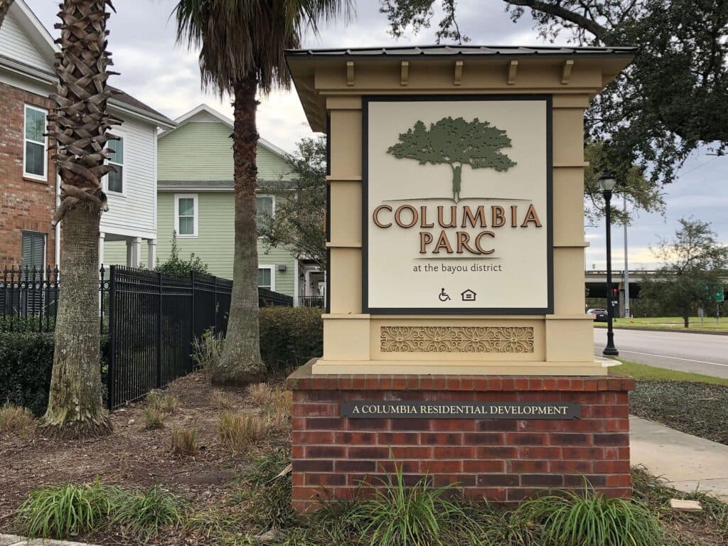 Sign for Columbia Parc at the Bayou District, a residential development, surrounded by greenery and palm trees.