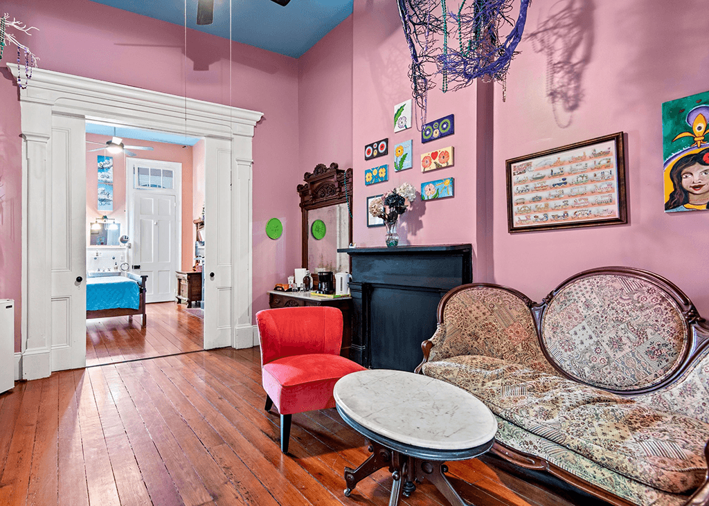 A cozy room with pink walls, a vintage couch, a red chair, and decorative wall art.