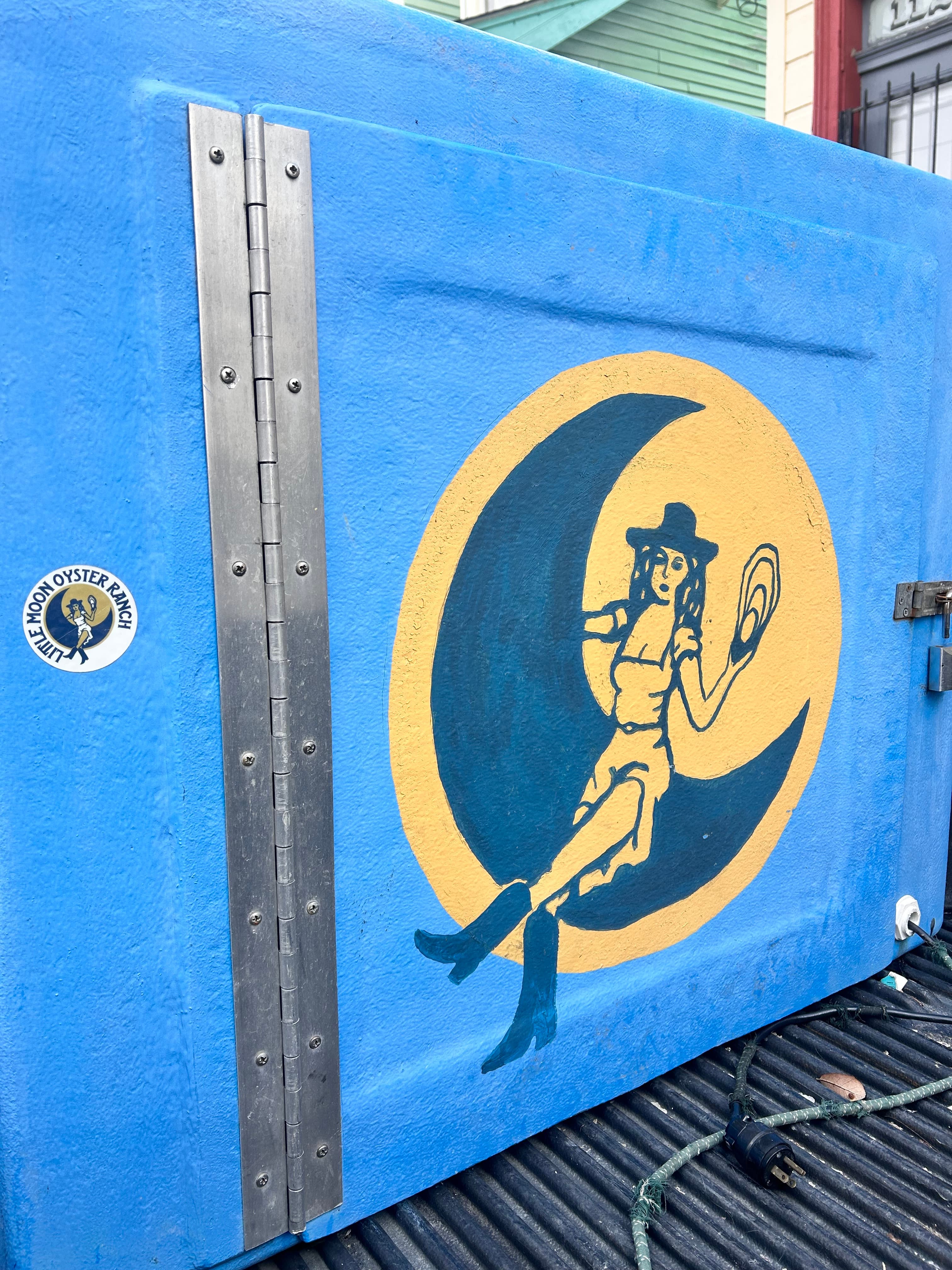 A blue cooler with a painted design of a woman holding an oyster in front of a crescent moon.