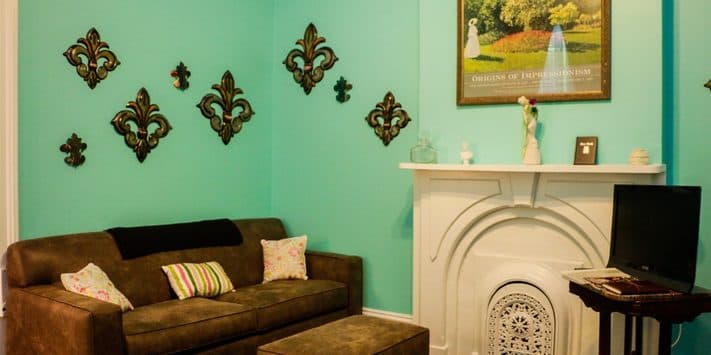 A cozy living room with a teal wall, a brown couch, decorative wall art, and a white fireplace.