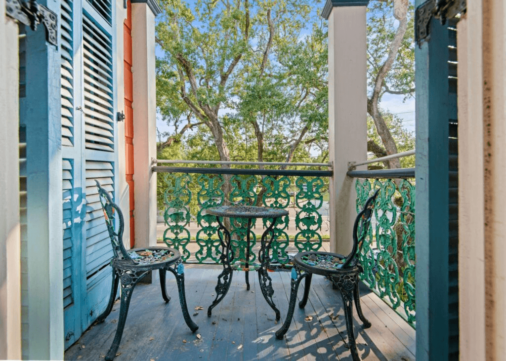 A small balcony features ornate metal chairs and table surrounded by greenery.