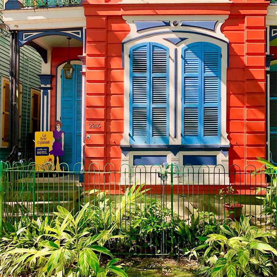 Colorful house with blue shutters, a green fence, and a sign for a hotel.