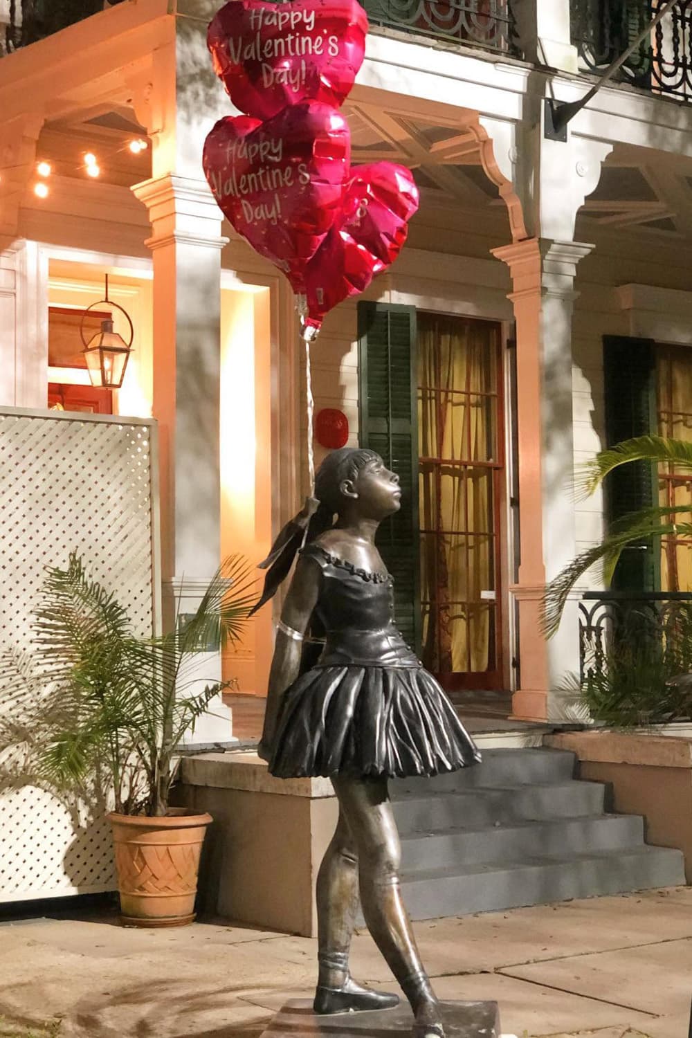 A bronze statue of a young girl in a dress holds heart-shaped balloons that read "Happy Valentine's Day!"