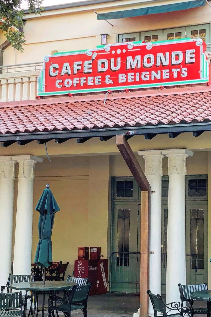 Cafe du Monde sign featuring coffee and beignets, with outdoor seating visible.
