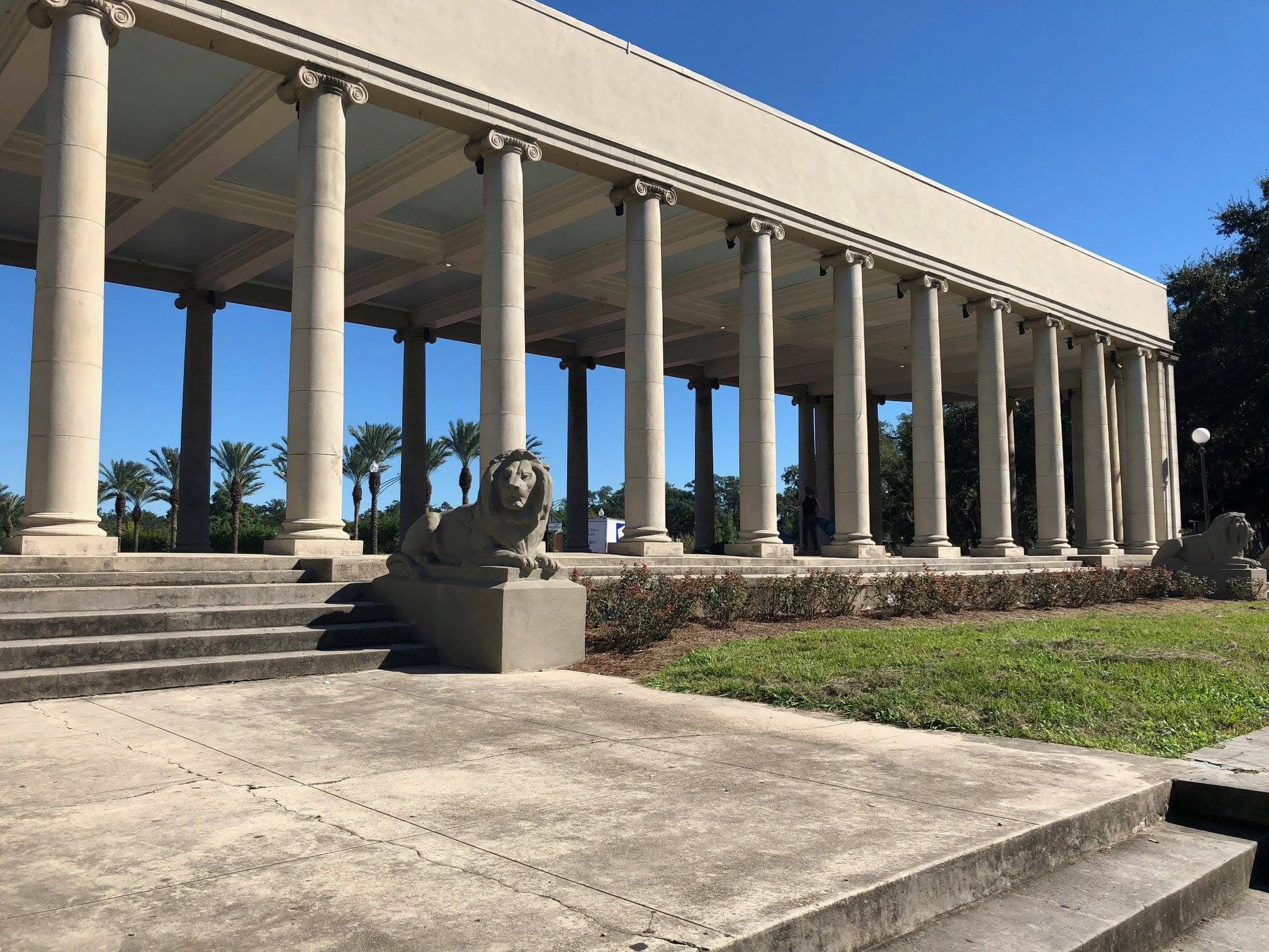 A colonnaded building with a lion statue in front, set against a clear blue sky.