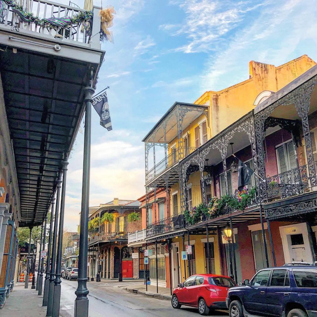 A picturesque street in New Orleans featuring colorful historic buildings and ornate iron balconies under a blue sky.