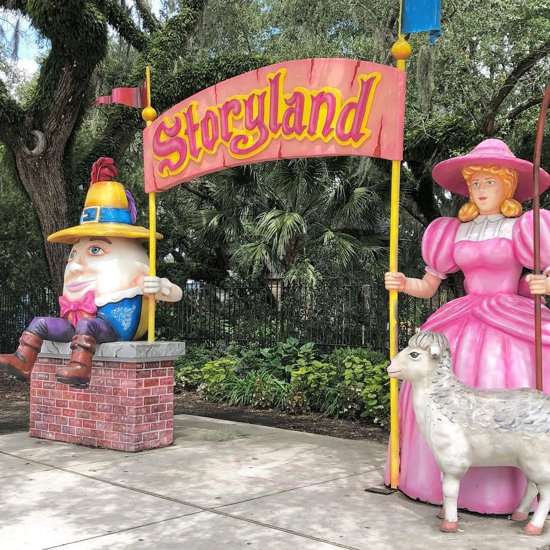 A whimsical entrance to Storyland featuring colorful characters, including a gnome and a woman in a pink dress, alongside a sheep.