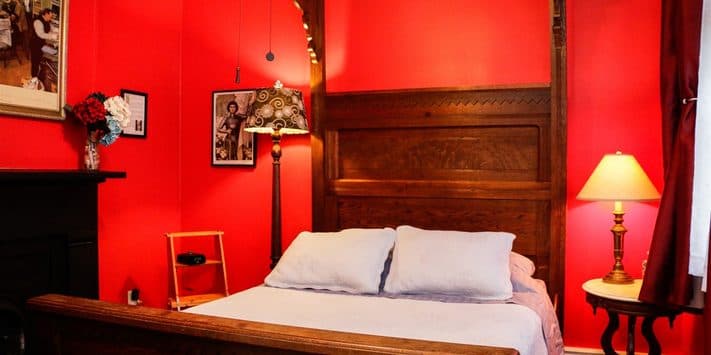 A cozy bedroom with a wooden bed, red walls, a decorative lamp, and framed art.