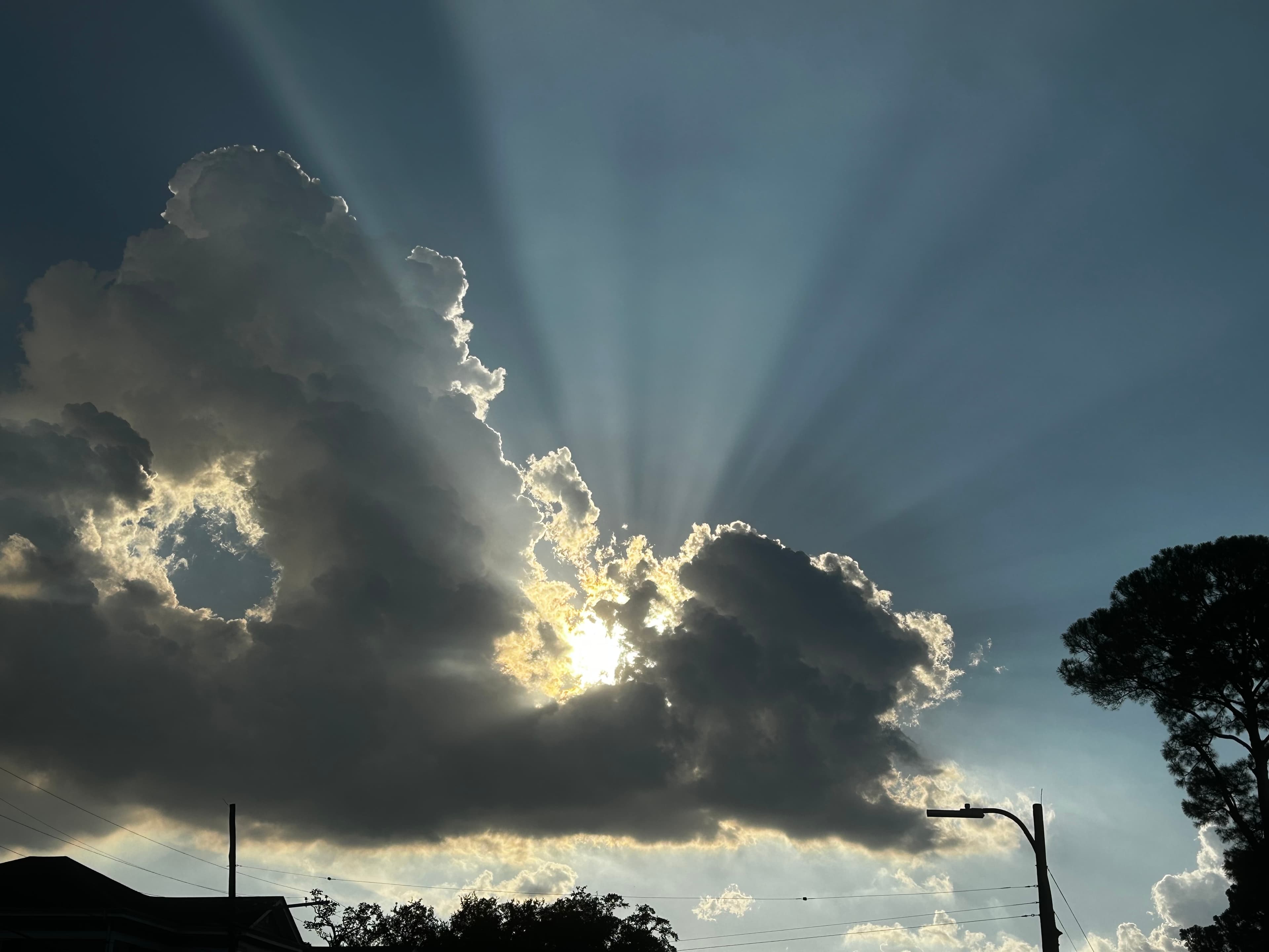 Sunlight beams radiate from behind a clouded sky.