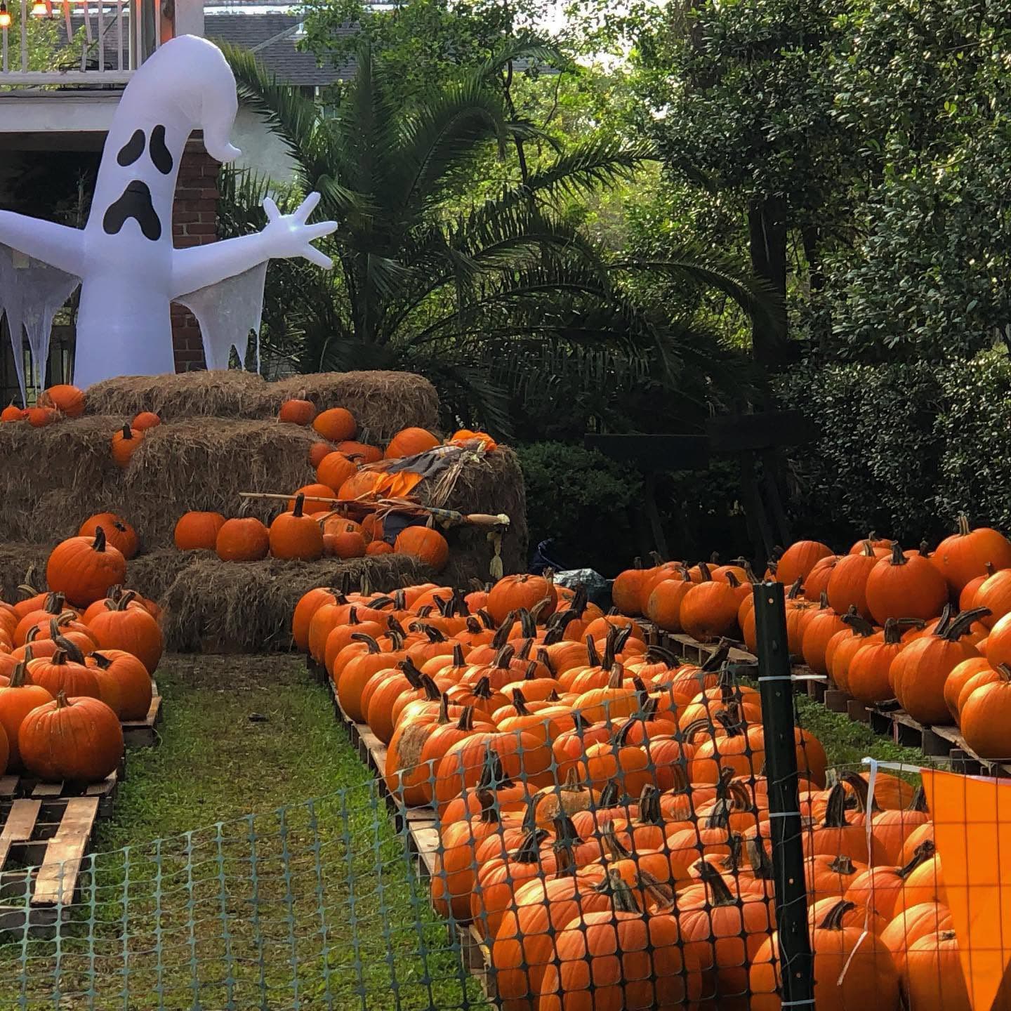 A large inflatable ghost stands among a display of pumpkins and hay bales in a festive outdoor setting.