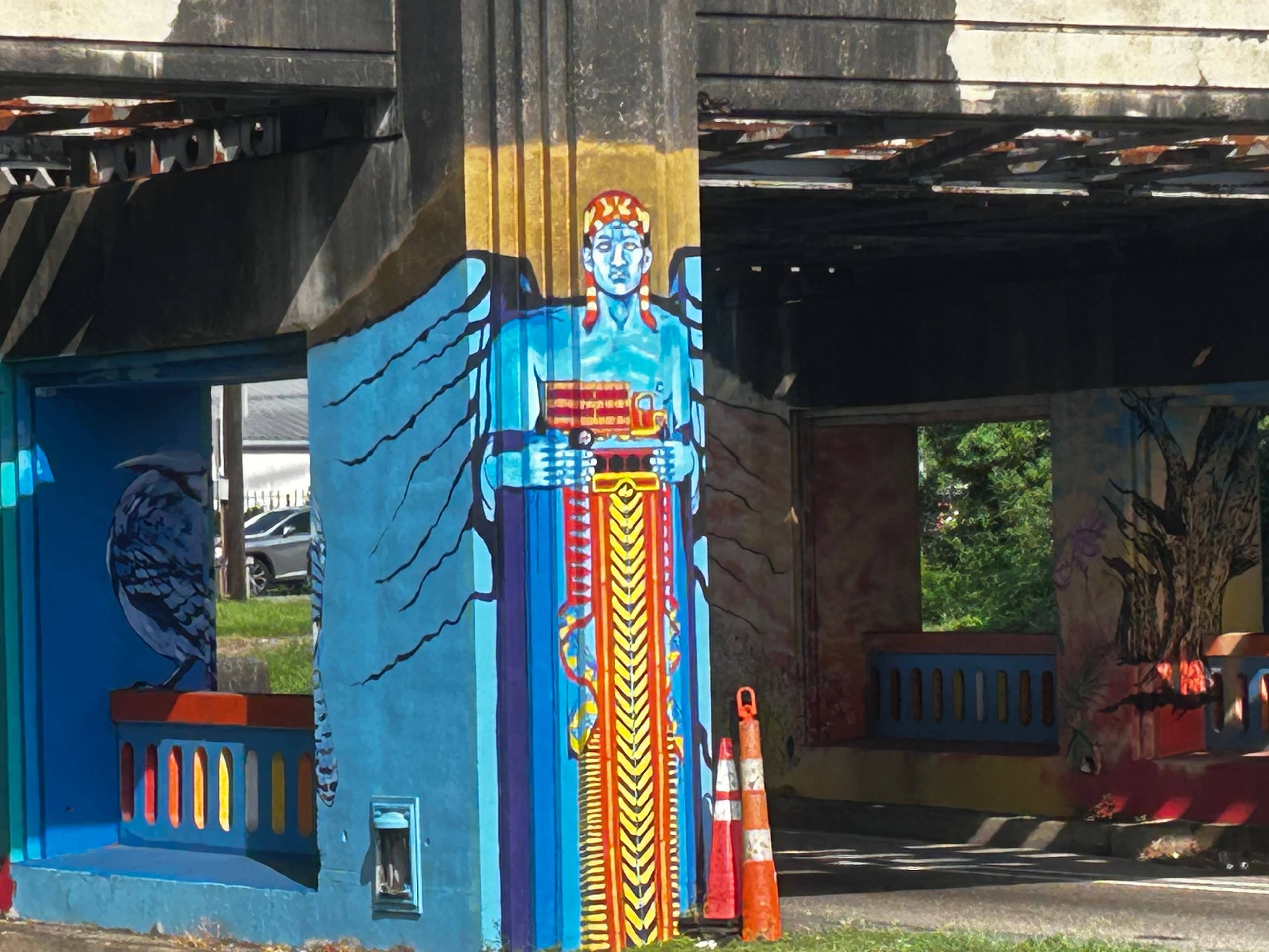 Vibrant mural of a blue figure with intricate details on a bridge support, surrounded by colorful patterns and textures.