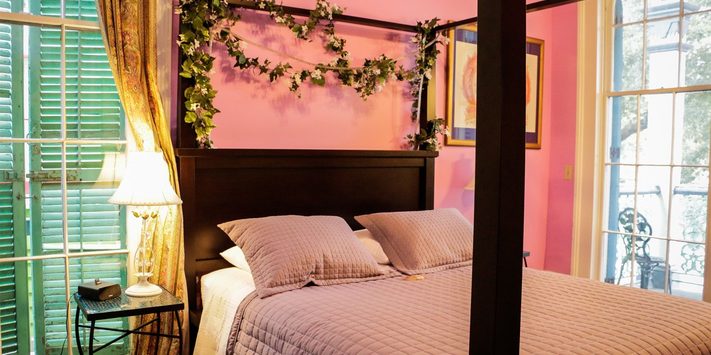 A cozy bedroom featuring a four-poster bed with pink walls and green shutters.