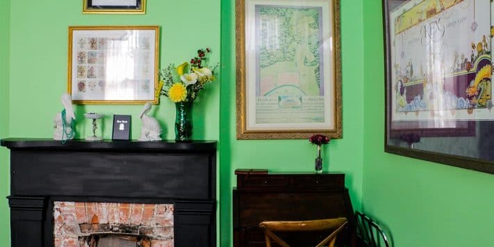 A bright green room featuring a black fireplace, framed artwork, a chair, and a vase of flowers.