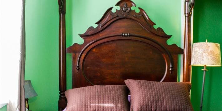 A vintage wooden bed frame with a green wall and two brown pillows.