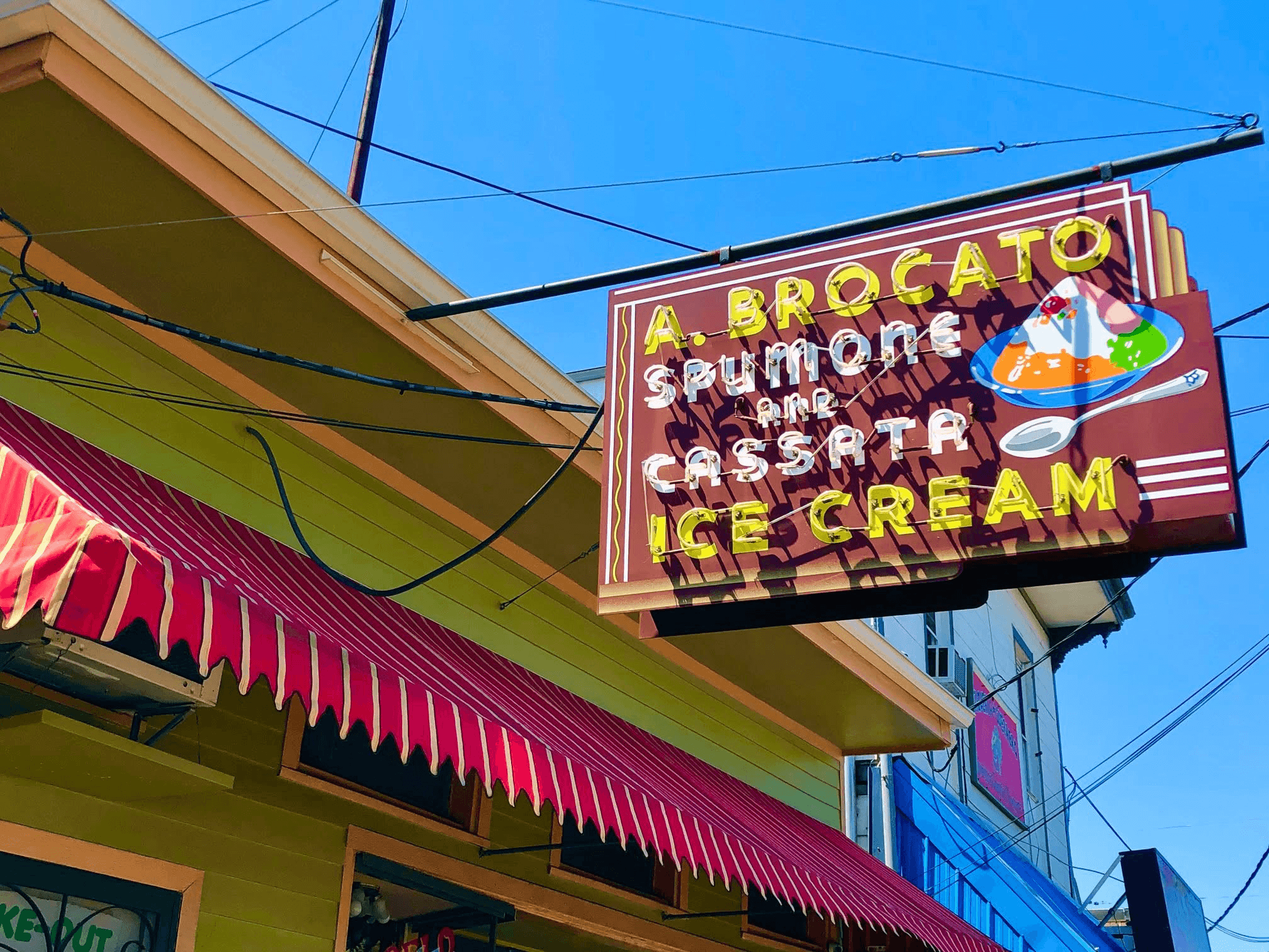Sign for A. Brocato Ice Cream, featuring flavors like spumoni and cassata, against a bright blue sky.