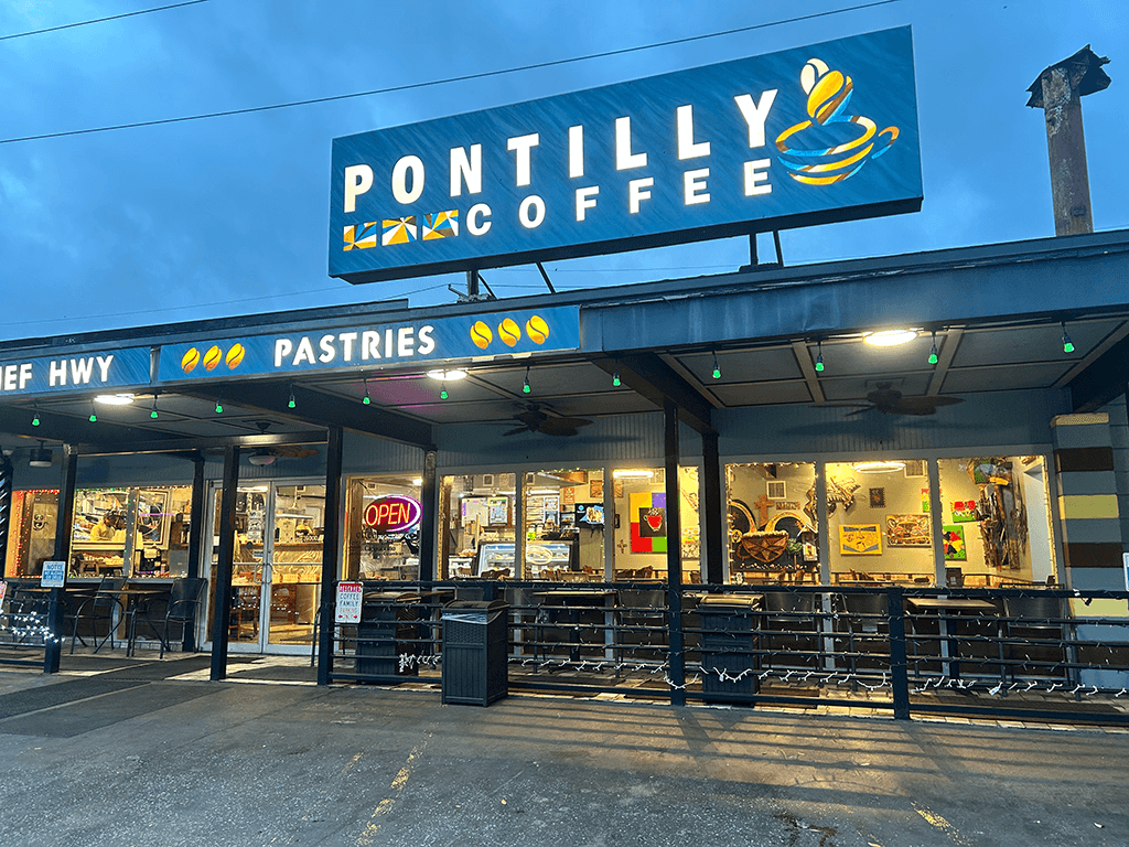 Exterior of Pontilly Coffee shop at dusk, featuring a brightly lit sign and outdoor seating.