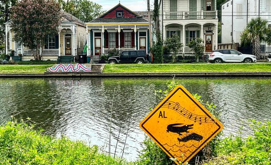 A canal lined with colorful houses features a humorous warning sign about singing alligators.