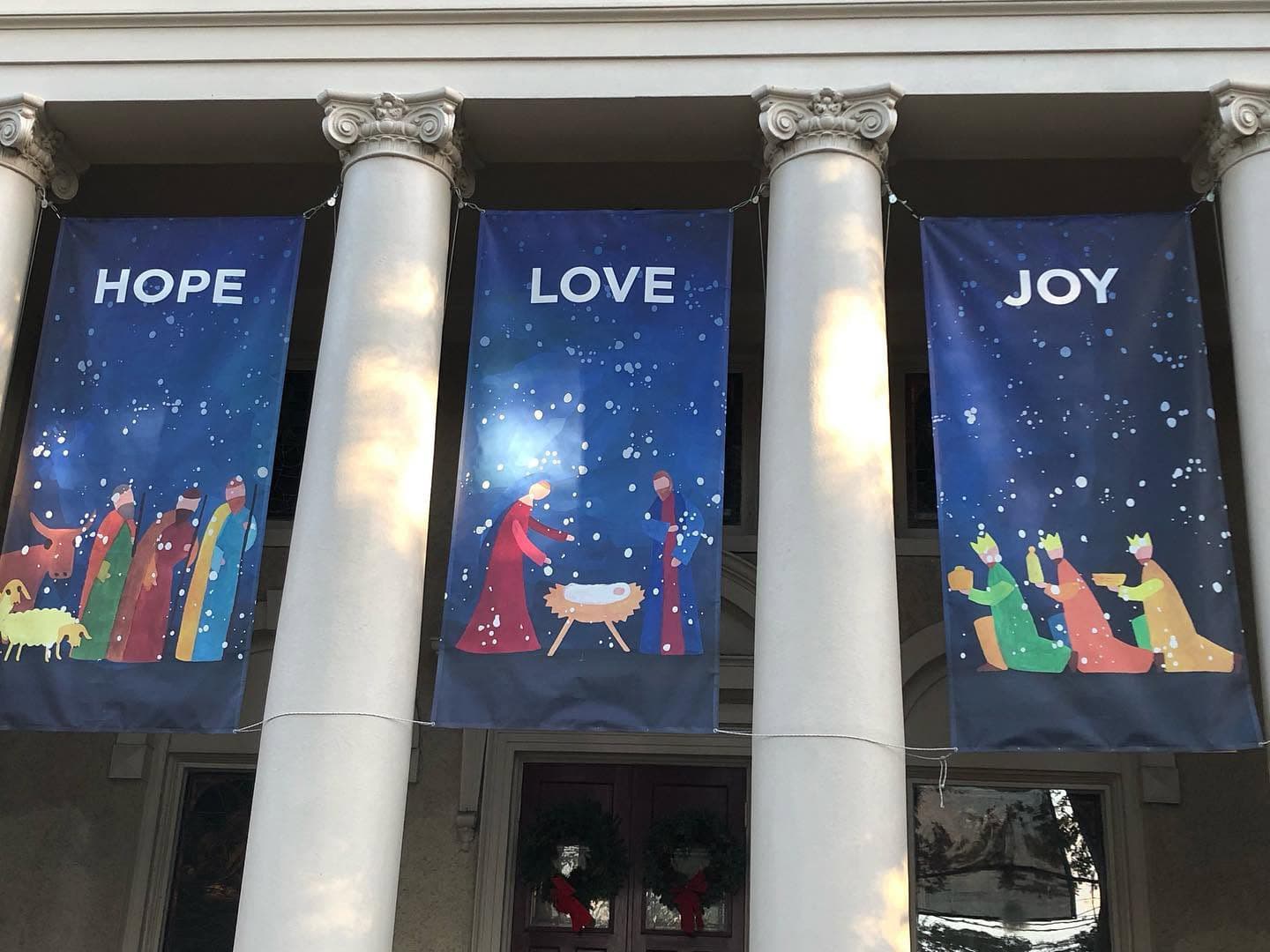Banners displaying the words "HOPE," "LOVE," and "JOY," alongside colorful nativity scenes, hang from columns.