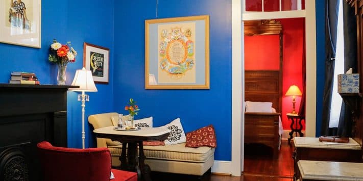 Cozy room with blue walls, a vintage sofa, decorative artwork, and a glimpse of a red bedroom area.
