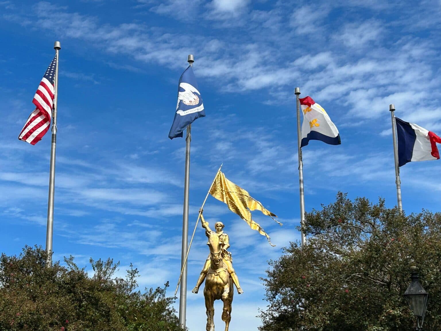 A golden statue of a mounted figure holding a flag stands among several flags under a blue sky.