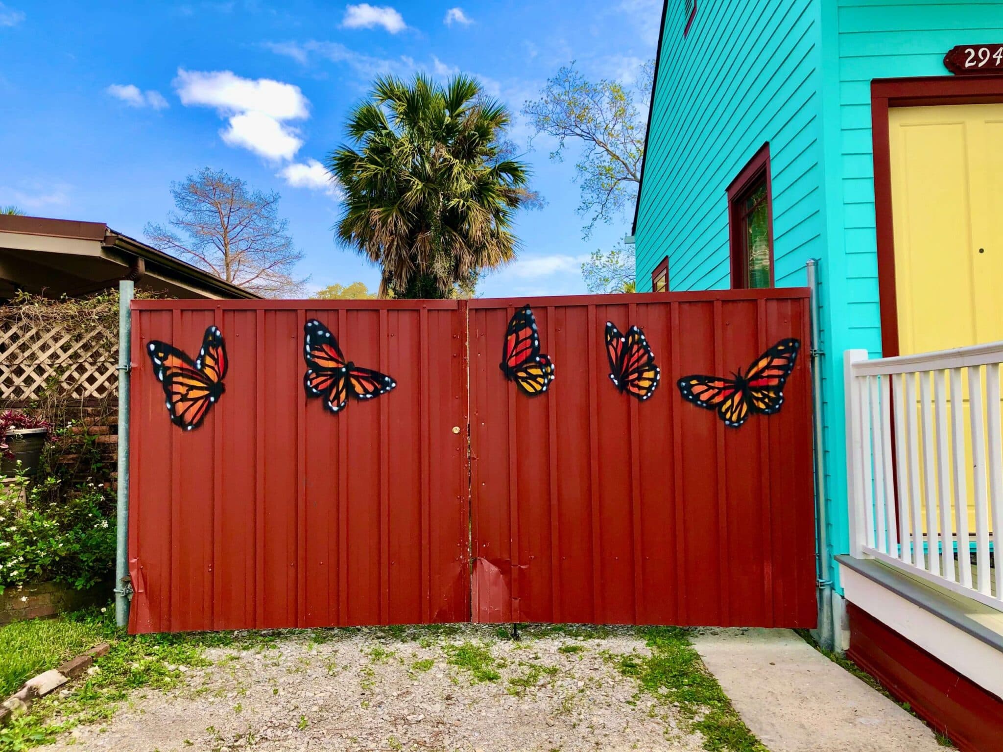 A red metal gate decorated with colorful butterfly cutouts, adjacent to a turquoise house. A red metal gate decorated with colorful butterfly cutouts, adjacent to a turquoise house.