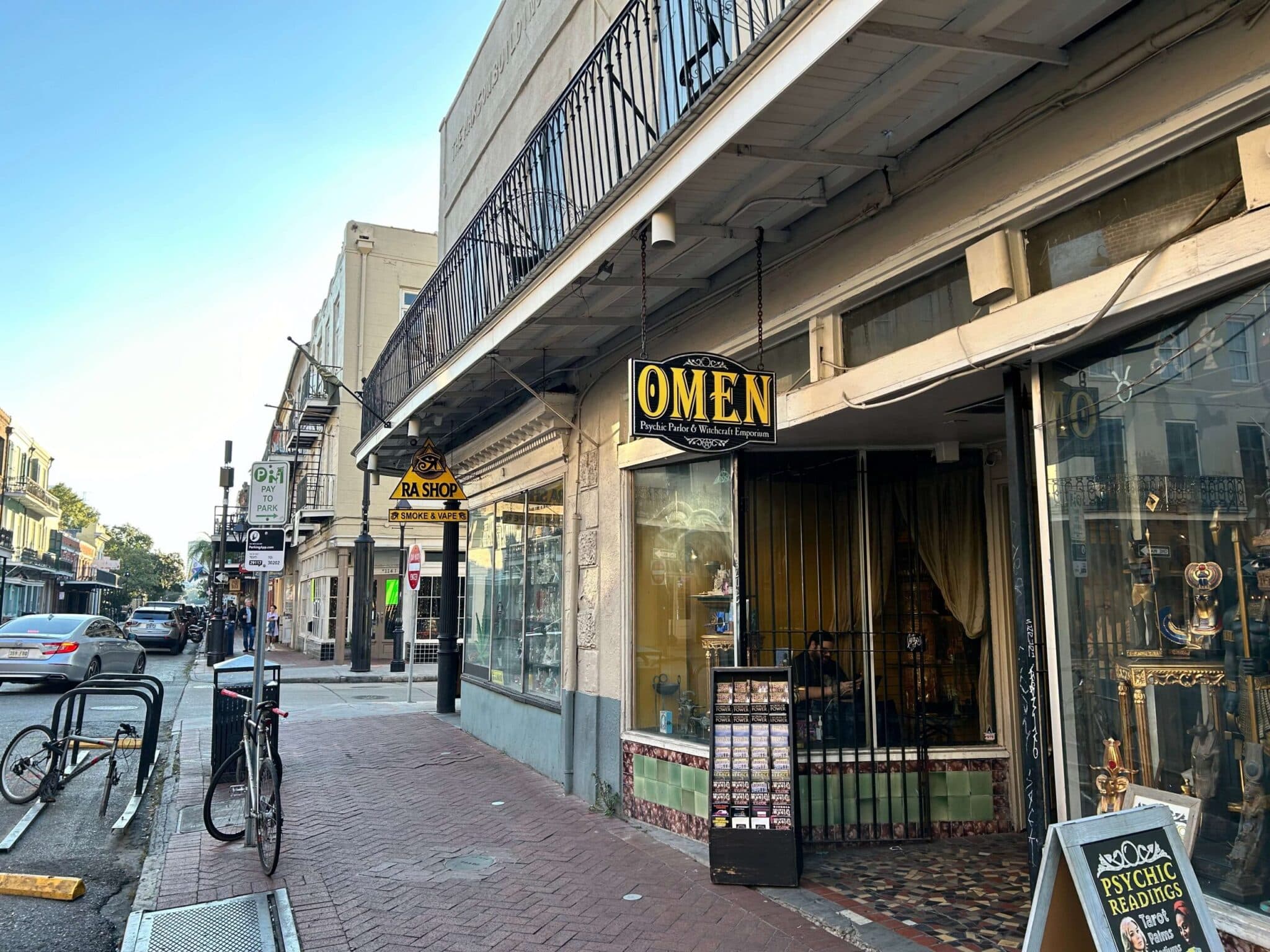 A streetscape features a psychic shop named "OMEN" with a decorative sign, situated alongside a narrow sidewalk. A streetscape features a psychic shop named "OMEN" with a decorative sign, situated alongside a narrow sidewalk.